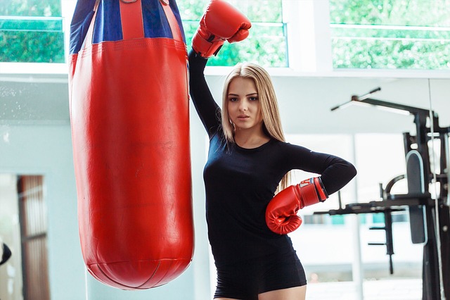 Žena v čiernom tričku s boxerskými rukavicami vedľa boxovacieho mechu.jpg